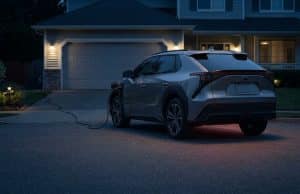 Rappel park outside : le danger d’incendie des véhicules en 2026 Une voiture électrique grise stationnée en extérieur et branchée sur une prise domestique devant une maison la nuit.