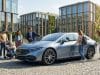 L’évolution du marché de la voiture électrique en 2026 Famille et professionnels autour d'une voiture électrique moderne devant un immeuble éco-conçu.