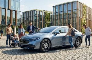 L’évolution du marché de la voiture électrique en 2026 Famille et professionnels autour d'une voiture électrique moderne devant un immeuble éco-conçu.