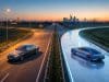 Quel avenir pour le moteur thermique et l’hybride en 2026 ? Une voiture thermique et une voiture électrique futuriste sur une autoroute séparée à l'approche d'une ville au coucher.
