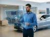 IA et prix voiture occasion : vers une cotation plus juste Un homme examine des données de marché sur une interface holographique devant une voiture dans une concession.