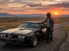 Burt Reynolds et sa Pontiac Trans Am : un accord de légende Un homme en chapeau de cowboy accoudé à une Pontiac Trans Am noire sur une route déserte au coucher du soleil.