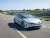 Tesla FSD en France : l’UTAC teste le système de Tesla Une berline électrique argentée roule sur autoroute, entourée de graphiques holographiques illustrant la conduite autonome.