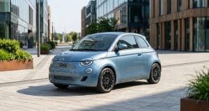 Pourquoi le prix dacia spring 2 est-il le plus bas du marché ? Une Fiat 500 électrique bleu clair garée sur une place pavée entre des immeubles de bureaux modernes.