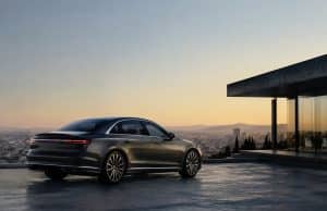 L’Audi A8 ne disparaîtra pas malgré des ventes faibles Une Audi A8 gris foncé stationnée sur une terrasse moderne surplombant une ville au coucher du soleil.