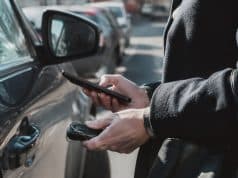Analyse d’un piratage informatique visant les données personnelles de centaines de milliers d’automobilistes français Gros plan sur une personne tenant un smartphone et une clé de voiture près d'un véhicule stationné dans la rue.