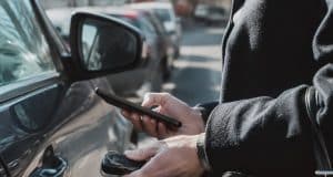 Analyse d’un piratage informatique visant les données personnelles de centaines de milliers d’automobilistes français Gros plan sur une personne tenant un smartphone et une clé de voiture près d'un véhicule stationné dans la rue.
