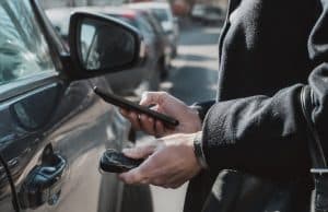 Analyse d’un piratage informatique visant les données personnelles de centaines de milliers d’automobilistes français Gros plan sur une personne tenant un smartphone et une clé de voiture près d'un véhicule stationné dans la rue.