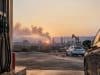 Carburants chers : votre permis pourrait coûter plus cher aux élèves Pompes à essence au premier plan avec une voiture et une raffinerie en arrière-plan sous un coucher de soleil.