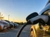 Les sept finalistes 100 % électriques de la Voiture de l’année 2027 (COTY) Gros plan sur un câble de recharge branché sur une voiture électrique avec d'autres véhicules garés en arrière-plan.