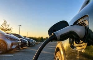 Les sept finalistes 100 % électriques de la Voiture de l’année 2027 (COTY) Gros plan sur un câble de recharge branché sur une voiture électrique avec d'autres véhicules garés en arrière-plan.
