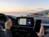 Android Auto : Google pourrait exclure les appareils sous Android 9 et 10 Conducteur tenant un smartphone dans sa main droite face au tableau de bord d'une voiture avec un système d'infodivertissement.