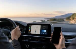 Android Auto : Google pourrait exclure les appareils sous Android 9 et 10 Conducteur tenant un smartphone dans sa main droite face au tableau de bord d'une voiture avec un système d'infodivertissement.