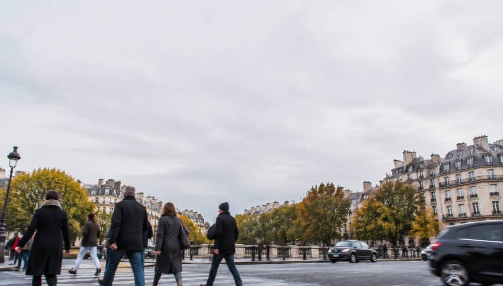 Piétons traversant une rue à Paris sur un passage clouté sous un ciel gris.